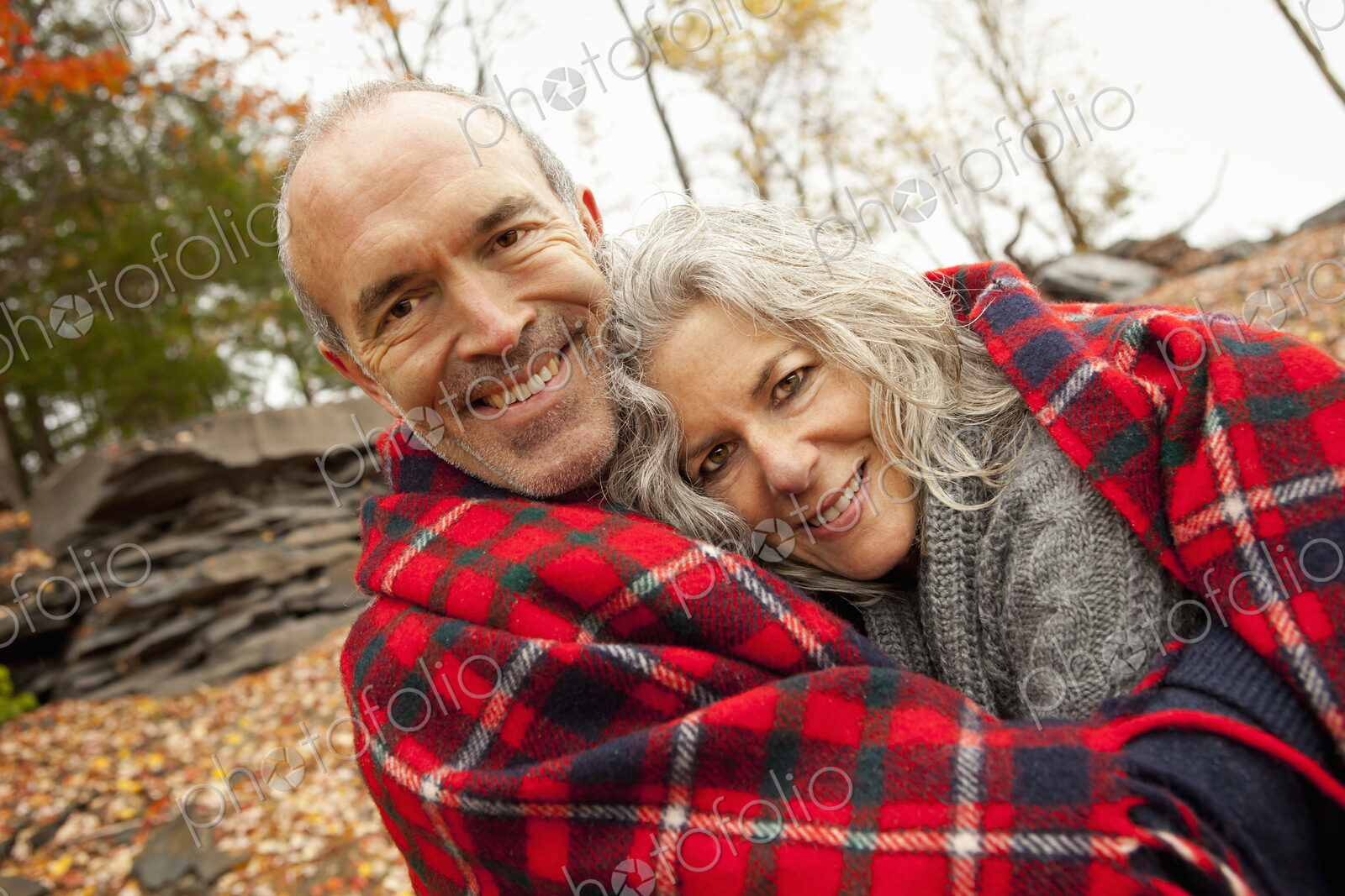 A couple, man and woman on a day out in autumn. Sharing a picnic rug to keep warm.