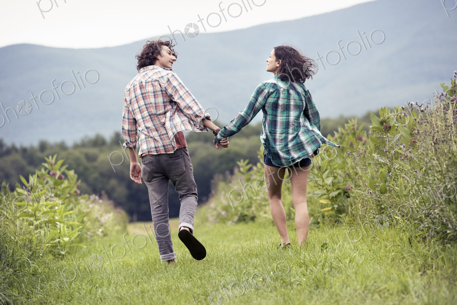 A couple, man and woman running through a meadow hand in hand.