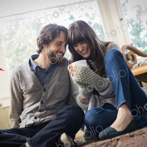 A couple, man and woman sitting close together warming up with their hands around mugs.