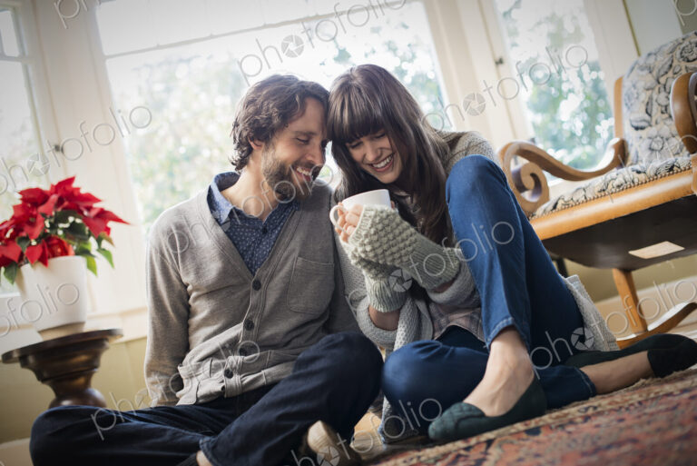 A couple, man and woman sitting close together warming up with their hands around mugs.