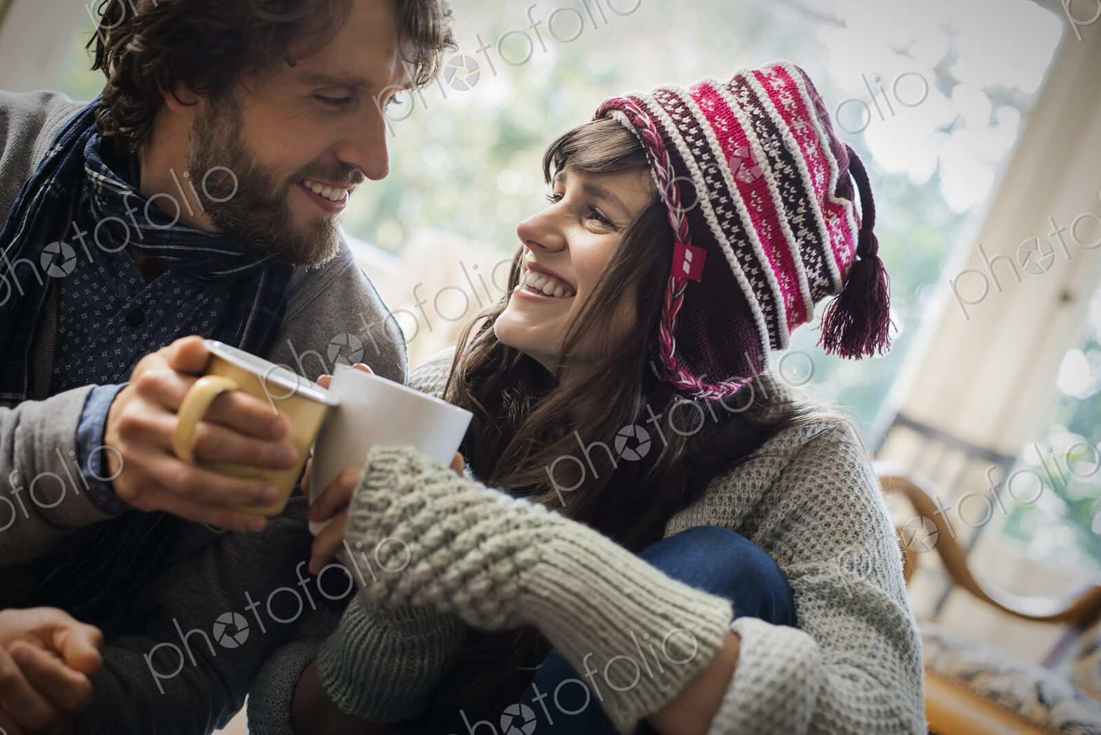 A couple, man and woman sitting close together warming up with their hands around mugs.
