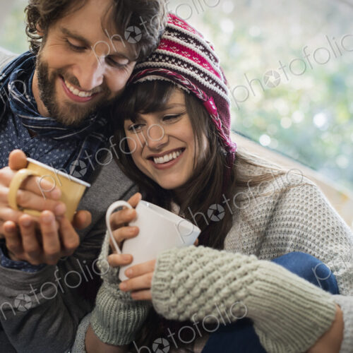 A couple, man and woman sitting close together warming up with their hands around mugs. A couple, man and woman sitting close together warming up with their hands around mugs.
