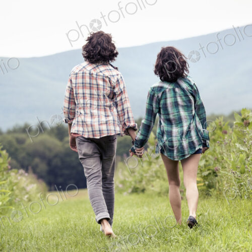A couple, man and woman walking through a meadow hand in hand, rear view. A couple, man and woman walking through a meadow hand in hand, rear view.