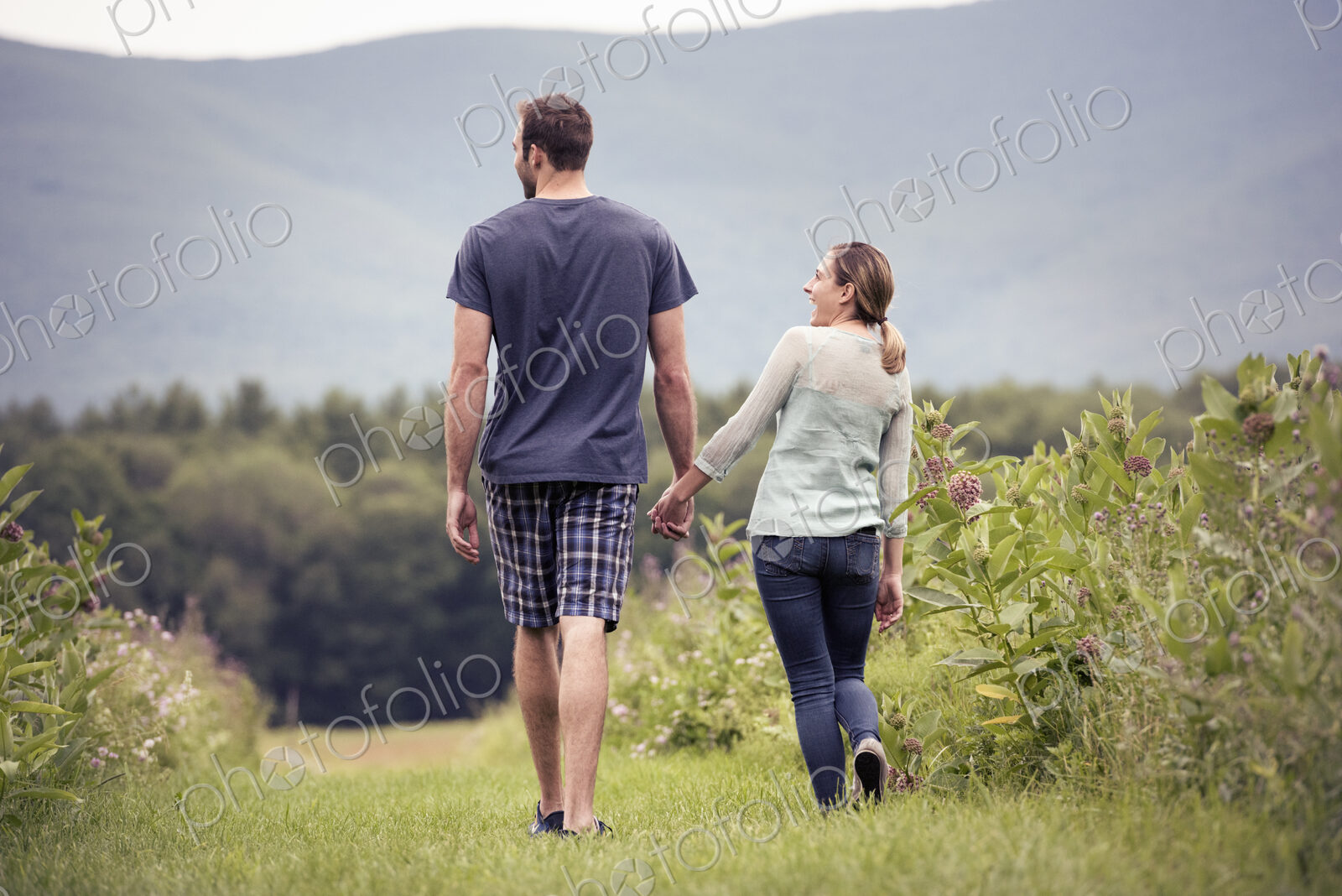 A couple, man and woman walking through a meadow holding hands.