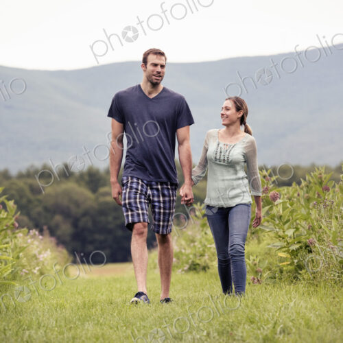 A couple, man and woman walking through a meadow holding hands.