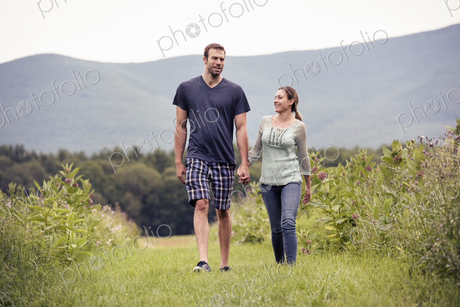 A couple, man and woman walking through a meadow holding hands.