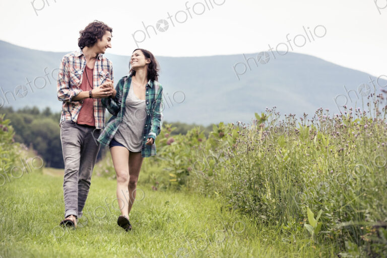 A couple, man and woman walking through a meadow in the countryside.
