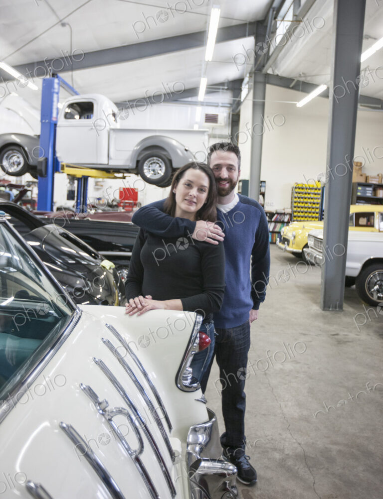 A couple, mechanics who work in a classic car auto repair shop. Man and woman.
