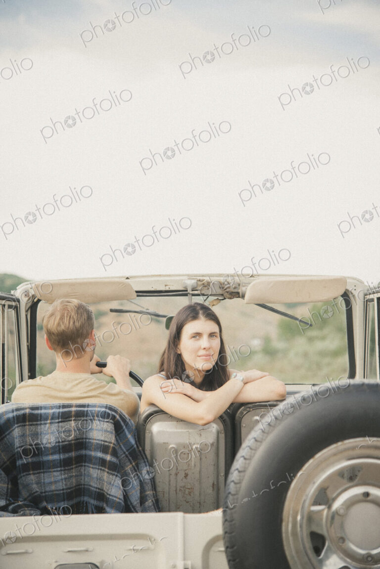 A couple on a road trip in a jeep side by side, a woman looking over her shoulder.