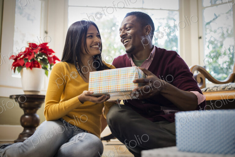 A couple on a sofa, exchanging wrapped presents.
