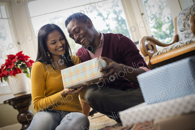 A couple on a sofa, exchanging wrapped presents.