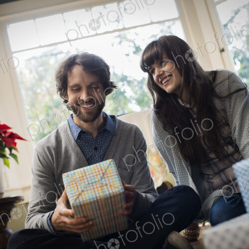 A couple on a sofa, exchanging wrapped presents.