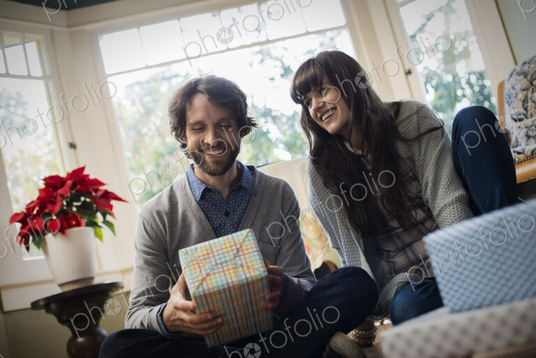 A couple on a sofa, exchanging wrapped presents.