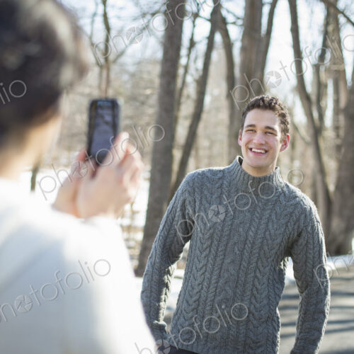 A couple outdoors on a snowy day. A woman holding a camera phone, taking photographs… A couple outdoors on a snowy day. A woman holding a camera phone, taking photographs…