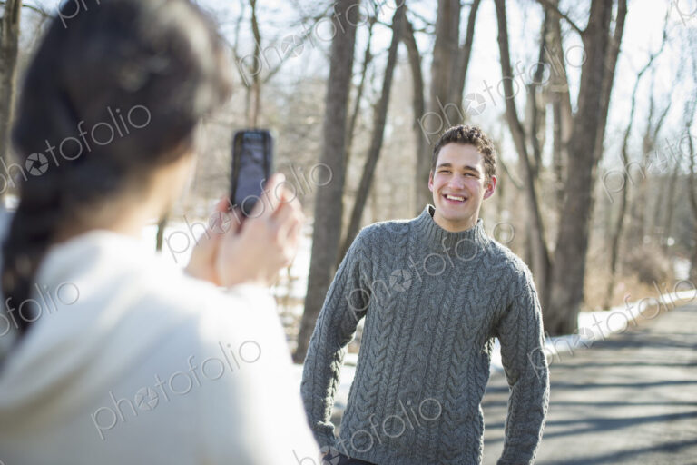 A couple outdoors on a snowy day. A woman holding a camera phone, taking photographs…
