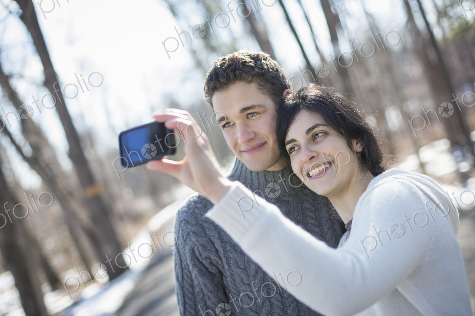 A couple outdoors on a snowy day. Woman holding a camera phone, taking photographs at…