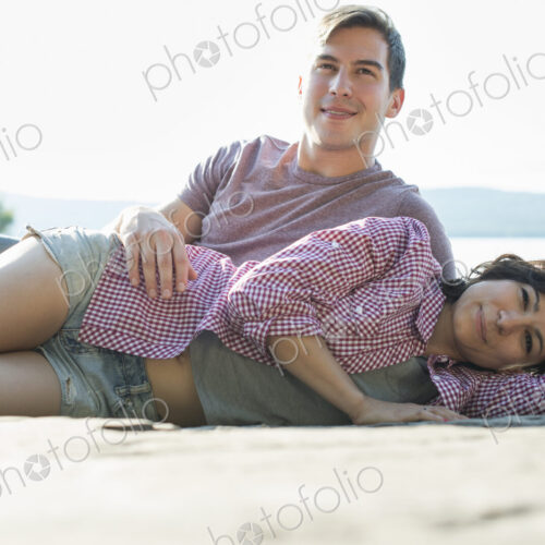 A couple relaxing, lying on a wooden jetty by a lake in summer.