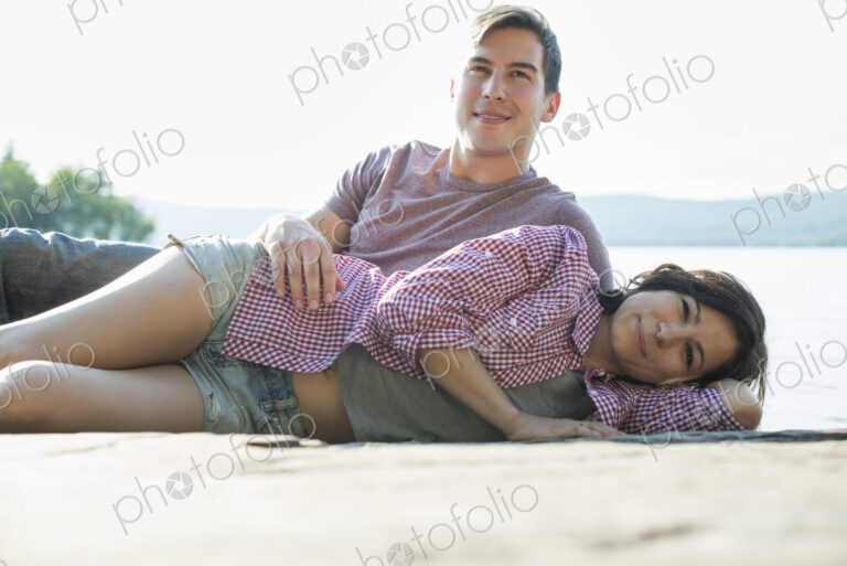 A couple relaxing, lying on a wooden jetty by a lake in summer.