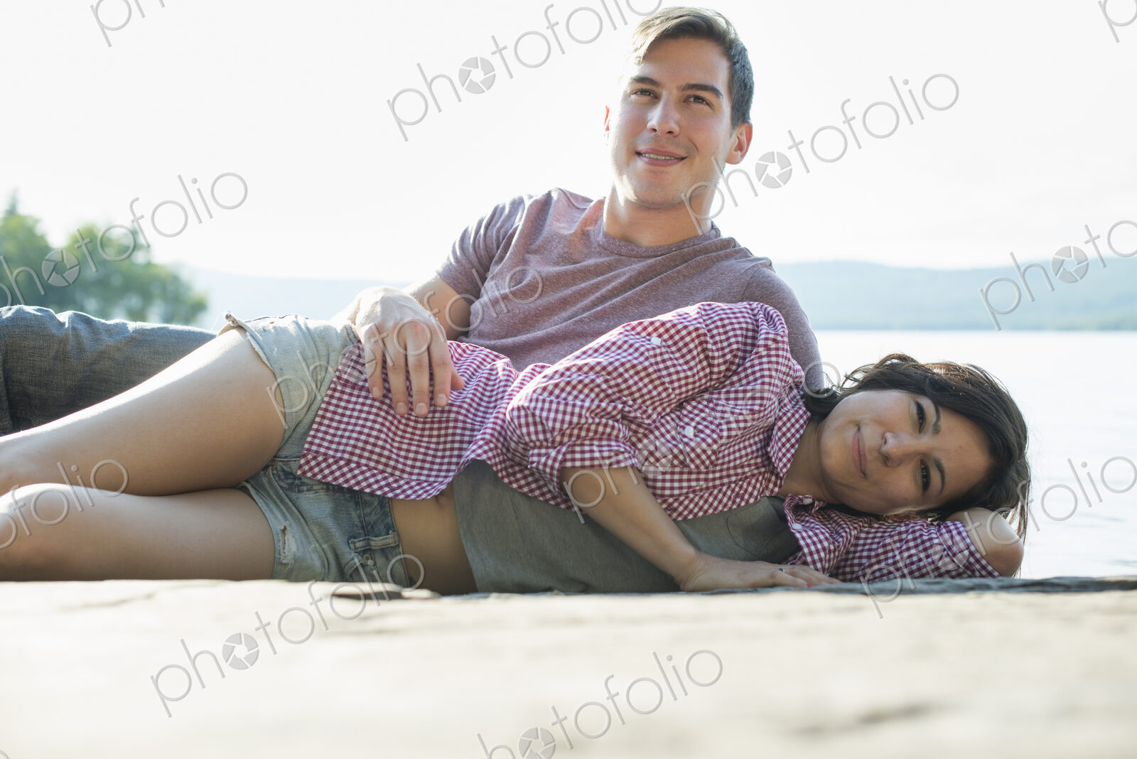 A couple relaxing, lying on a wooden jetty by a lake in summer.