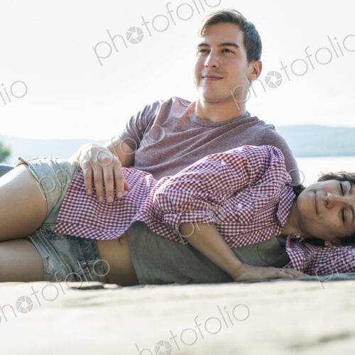 A couple relaxing, lying on a wooden jetty by a lake in summer.