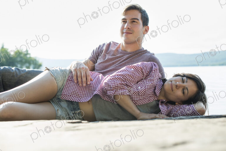 A couple relaxing, lying on a wooden jetty by a lake in summer.