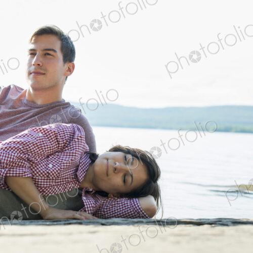 A couple relaxing, lying on a wooden jetty by a lake in summer.