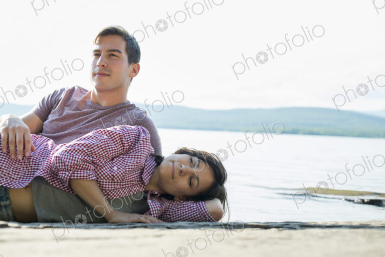 A couple relaxing, lying on a wooden jetty by a lake in summer.