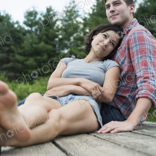 A couple relaxing on a jetty overlooking a mountain lake.