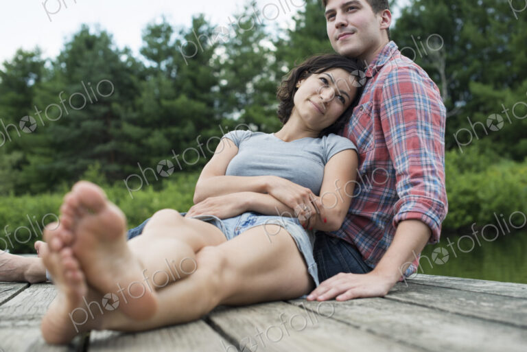 A couple relaxing on a jetty overlooking a mountain lake.
