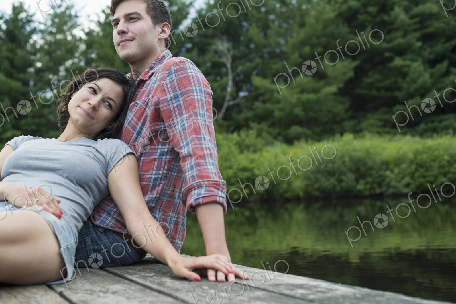 A couple relaxing on a jetty overlooking a mountain lake.