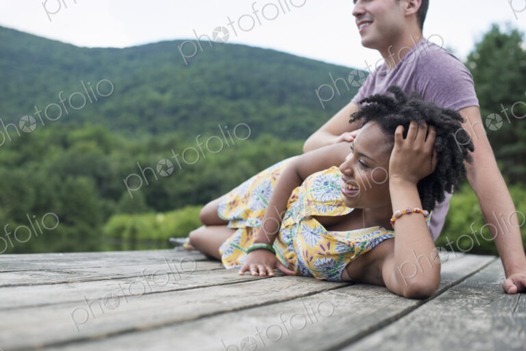 A couple relaxing on a jetty overlooking a mountain lake.