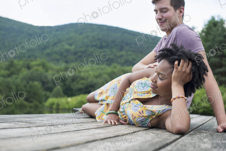 A couple relaxing on a jetty overlooking a mountain lake.