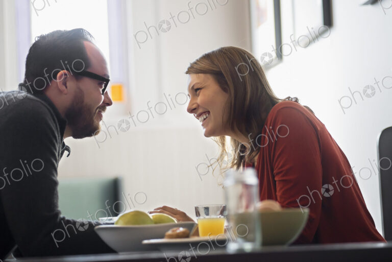 A couple sitting in a coffeeshop over breakfast. Leaning towards each other.