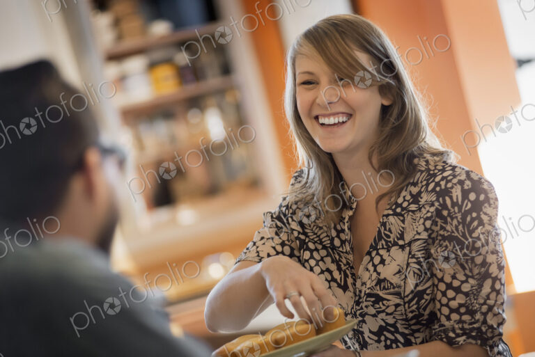 A couple sitting in a coffeeshop smiling and talking over a cup of coffee.