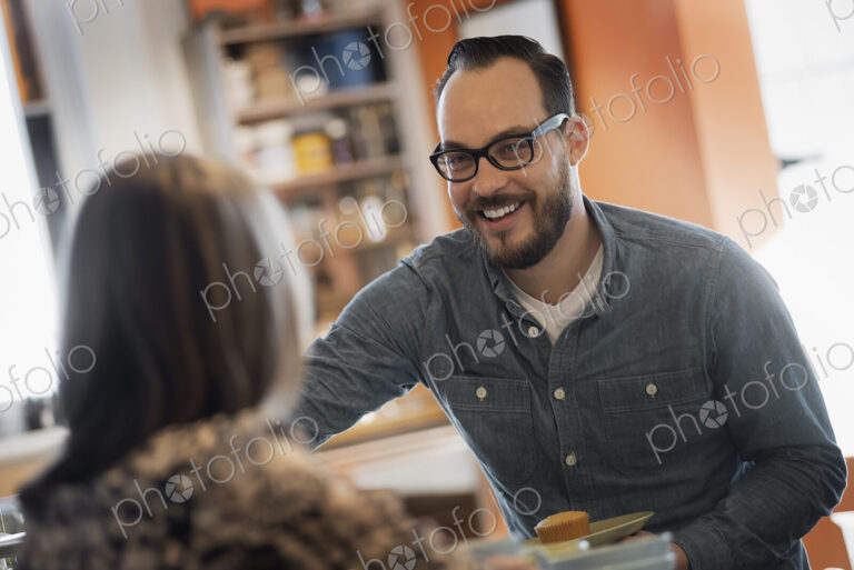 A couple sitting in a coffeeshop smiling and talking over a cup of coffee.