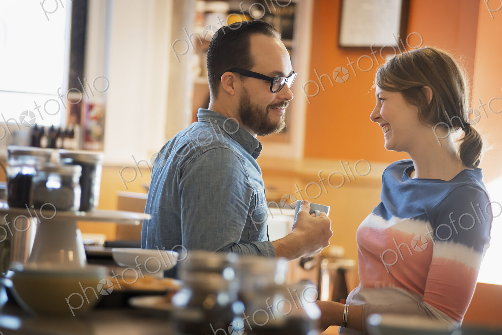 A couple sitting in a coffeeshop smiling and talking over a cup of coffee.
