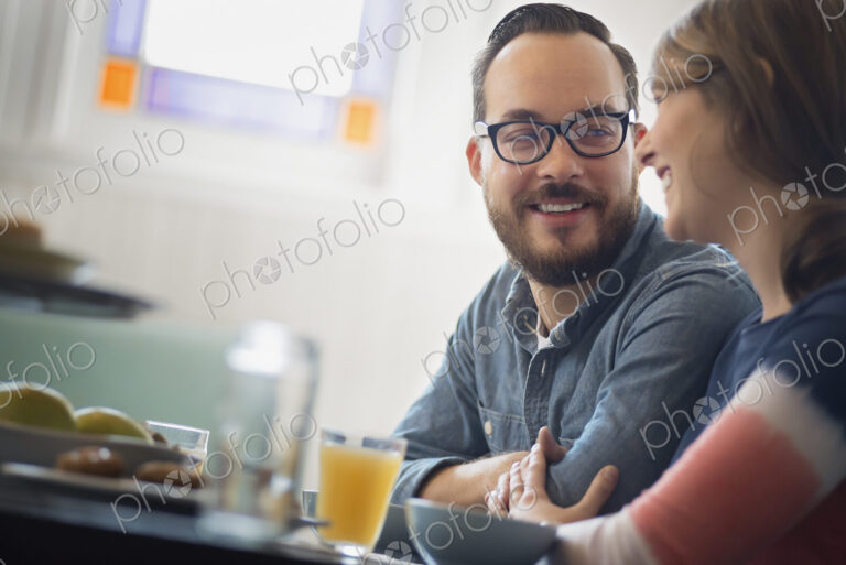 A couple sitting in a coffeeshop smiling and talking over a cup of coffee.