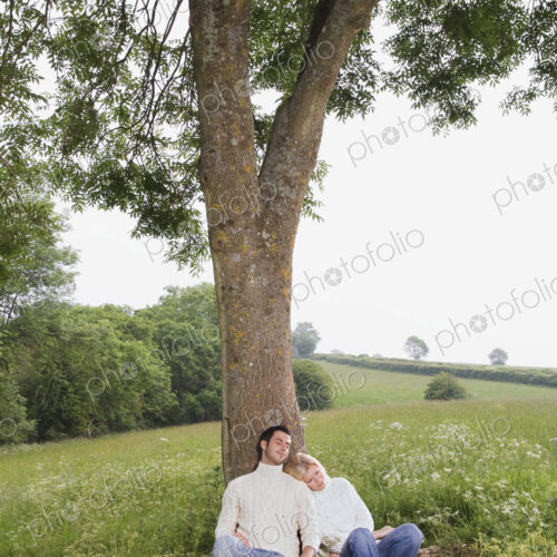 A couple sitting leaning against a tree in a meadow. A couple sitting leaning against a tree in a meadow.