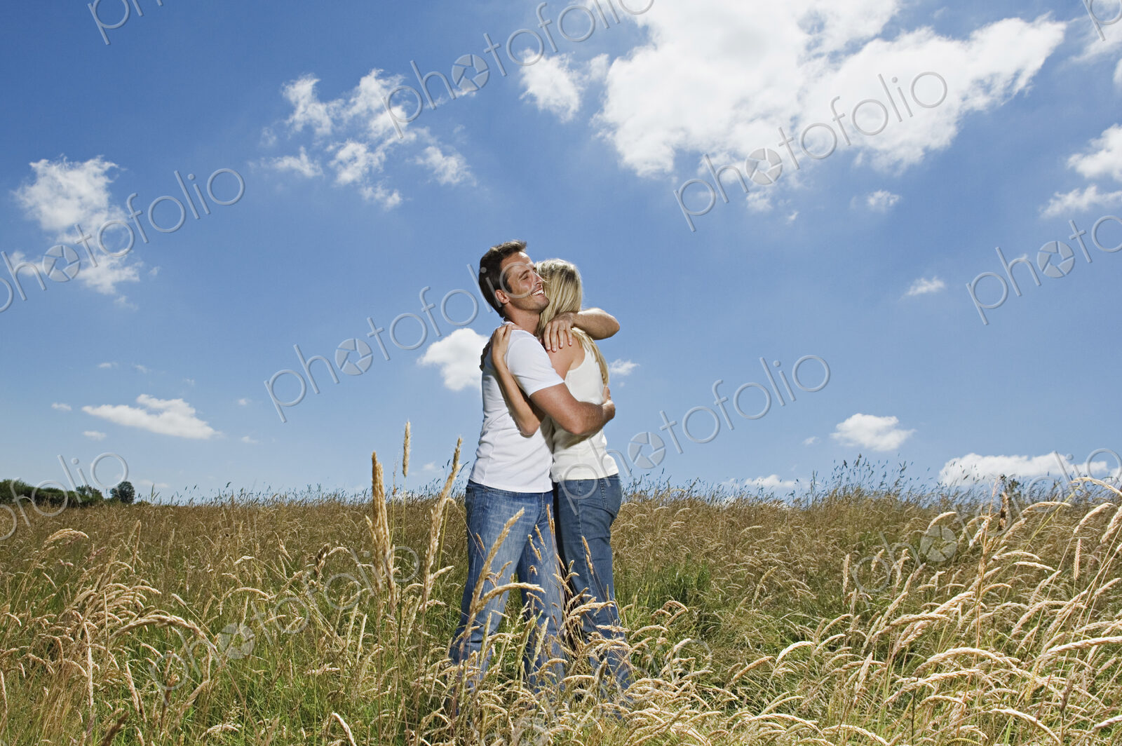 A couple standing in a field of wheat hugging.