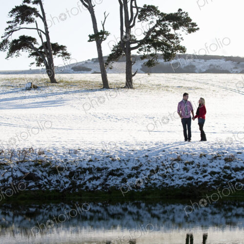 A couple standing in a snow-covered field by a river, holding hands. A couple standing in a snow-covered field by a river, holding hands.