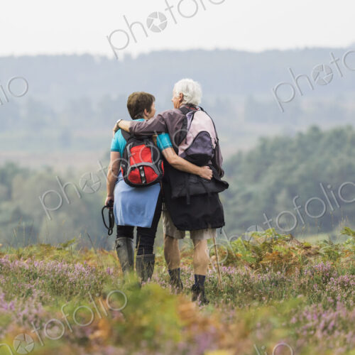 A couple standing on a path looking at the view over wooded hills, with arms around… A couple standing on a path looking at the view over wooded hills, with arms around…