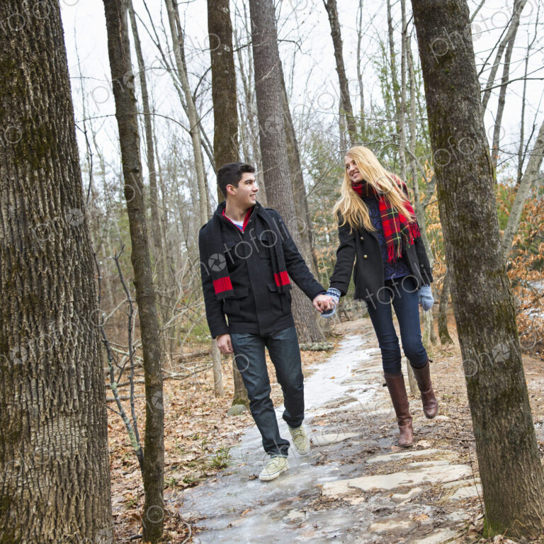 A couple walking hand in hand through a woodland in winter.