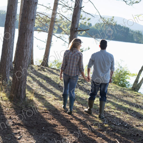 A couple walking in woodland on the shores of a lake. A couple walking in woodland on the shores of a lake.