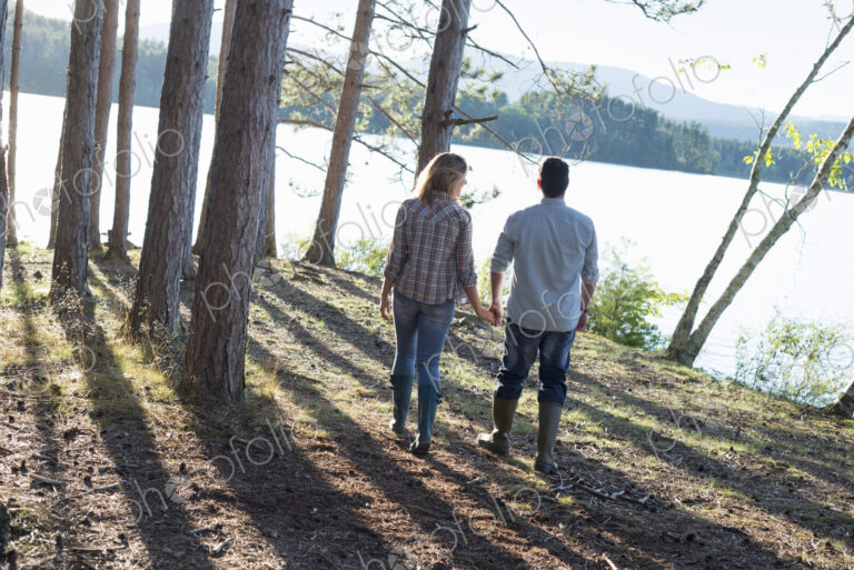A couple walking in woodland on the shores of a lake.