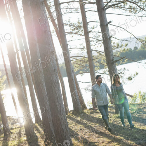 A couple walking in woodland on the shores of a lake. A couple walking in woodland on the shores of a lake.