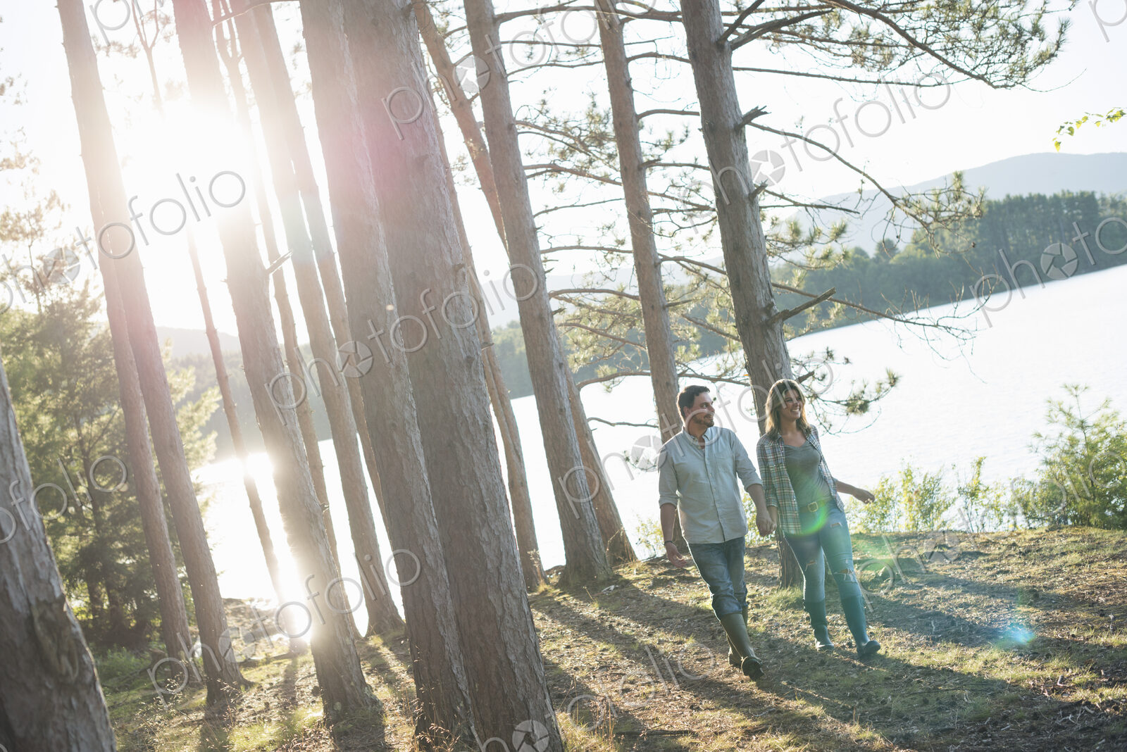 A couple walking in woodland on the shores of a lake.