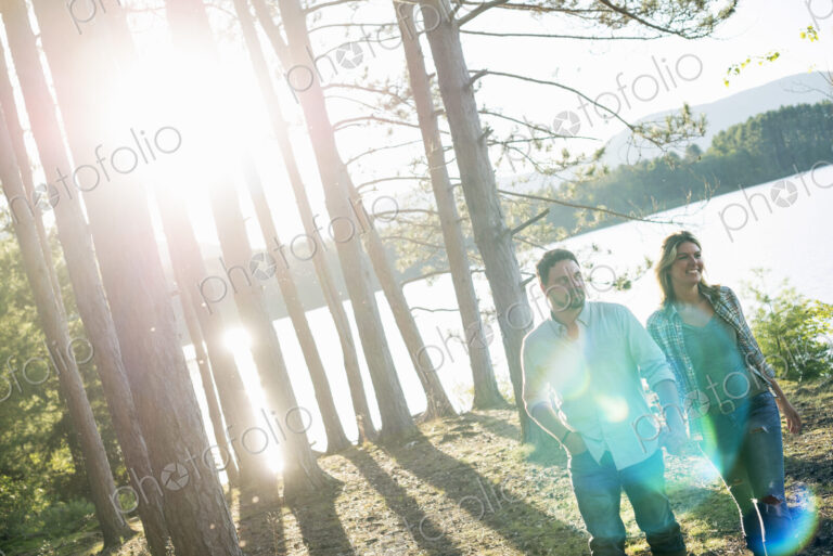 A couple walking in woodland on the shores of a lake.