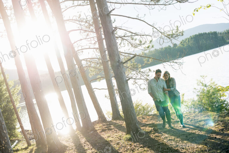 A couple walking in woodland on the shores of a lake.