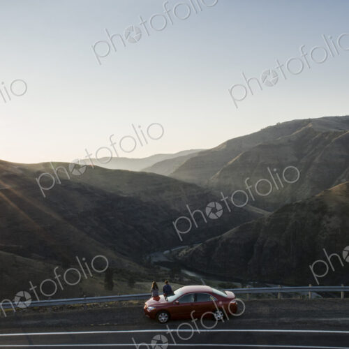 A couple watching the sunset standing next to their car at a rest stop
