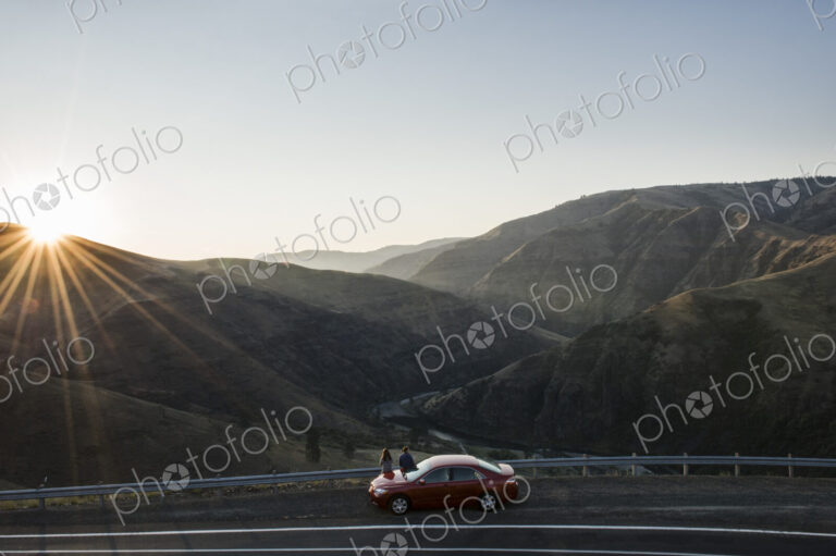 A couple watching the sunset standing next to their car at a rest stop